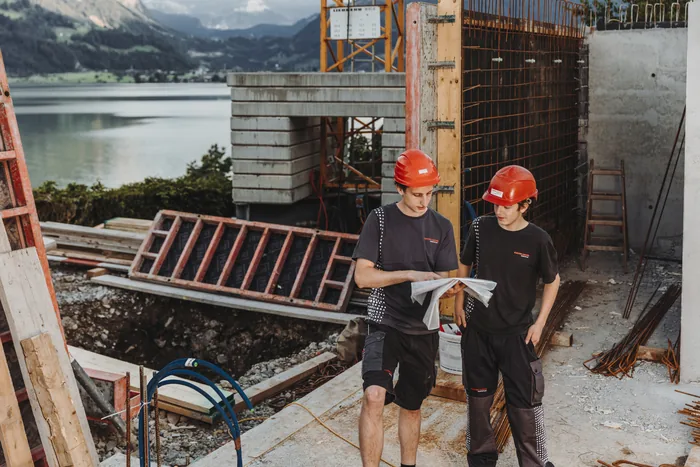 Zwei Baufachkräfte mit Schutzhelmen besprechen einen Plan auf einer Baustelle