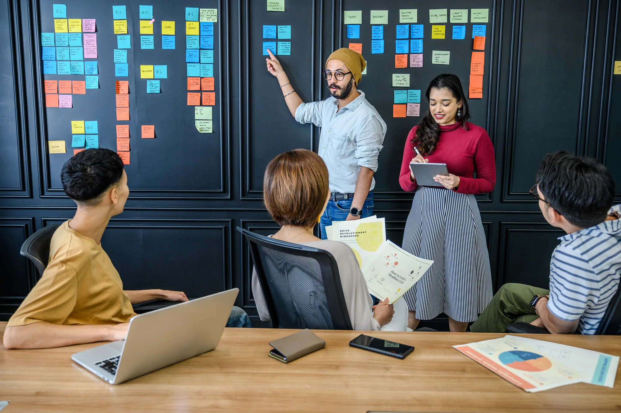 Ein Team bespricht einen Strategieplan mit bunten Haftnotizen an einer Bürowand.