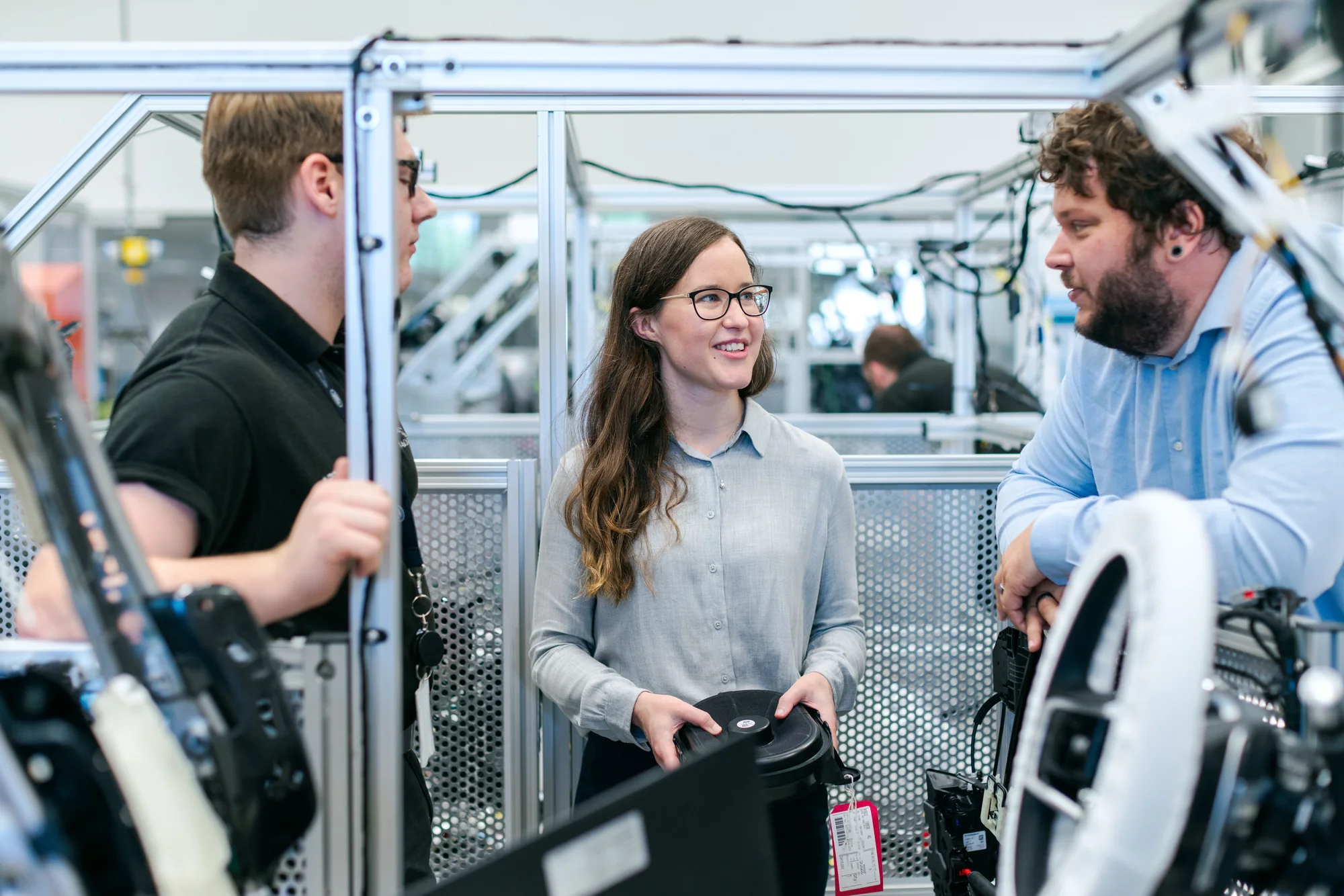 Drei Ingenieurinnen und Ingenieure sprechen neben Maschinen in einer technischen Werkstatt.