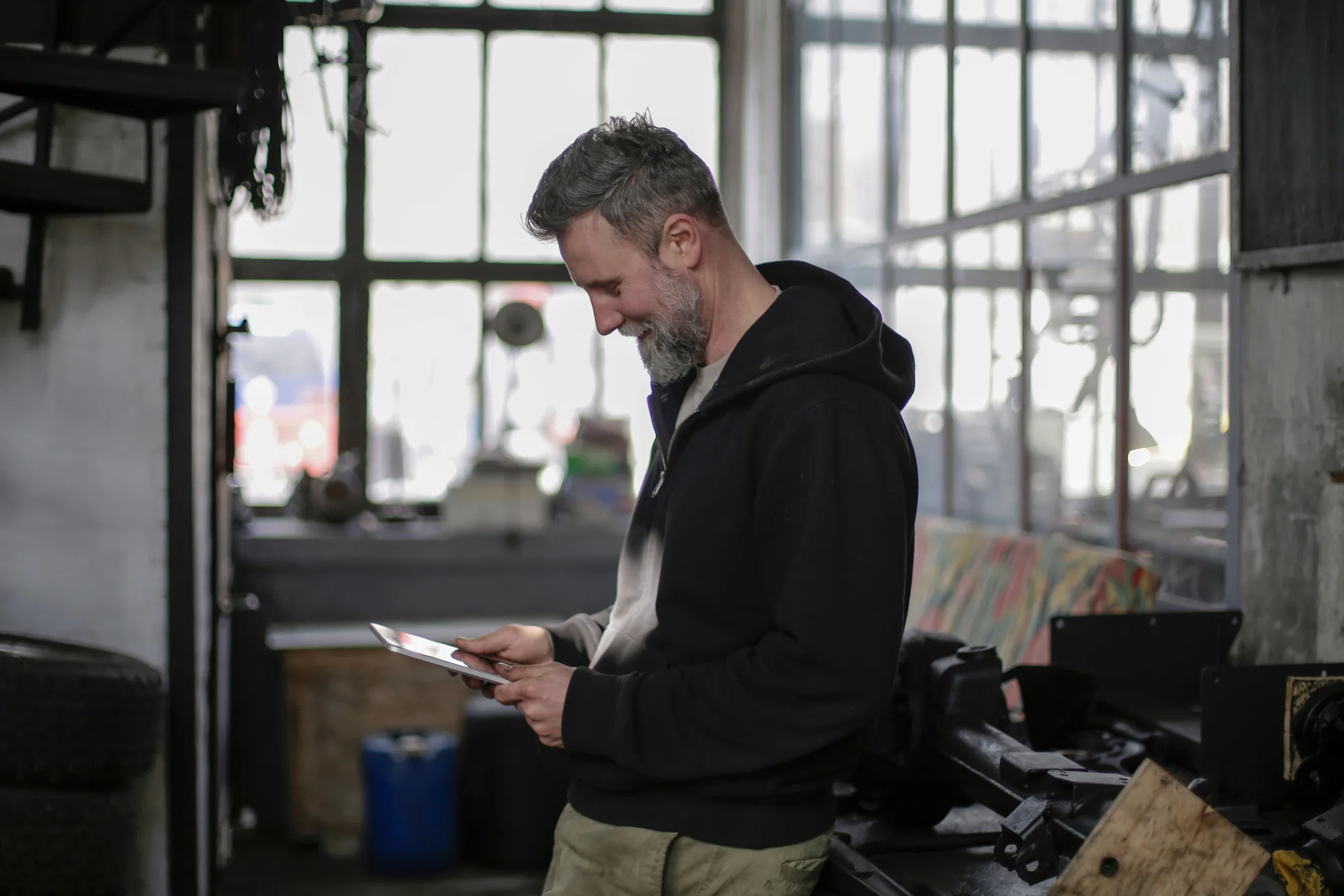 Ein Handwerker nutzt ein Tablet an der Werkbank in einer hellen Werkstatt.
