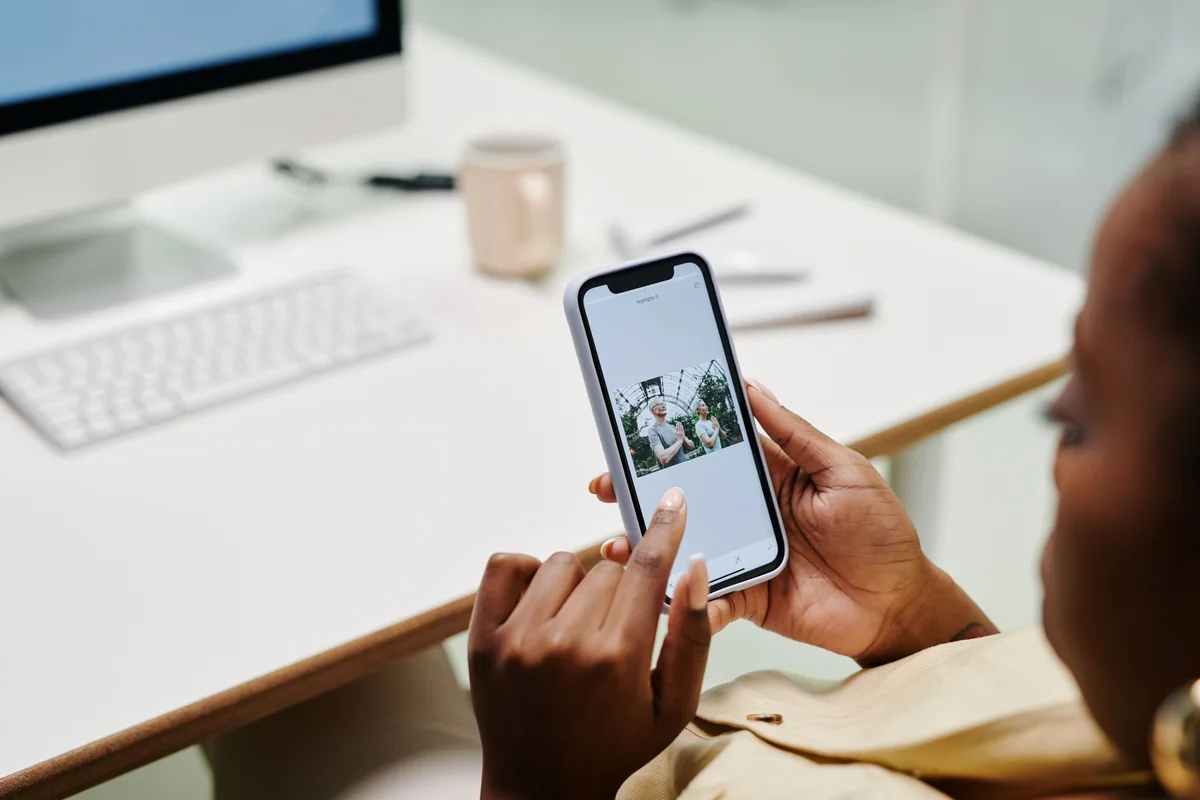 Nahaufnahme einer Person, die am Schreibtisch ein Smartphone mit beiden Händen bedient.