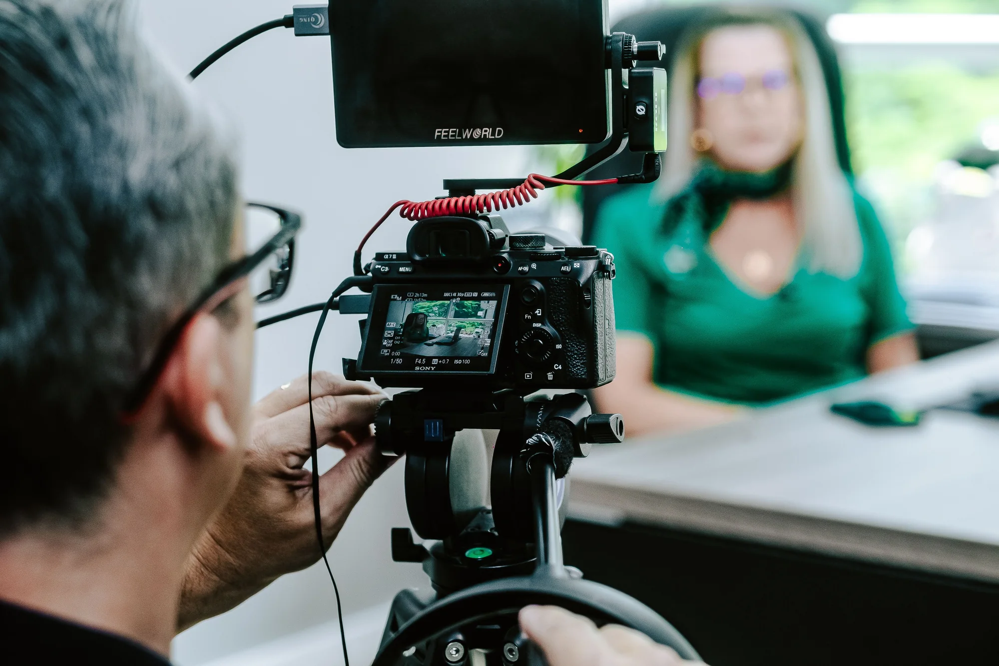 Ein Videograf filmt eine Frau bei einem Interview an ihrem Arbeitsplatz im Büro.